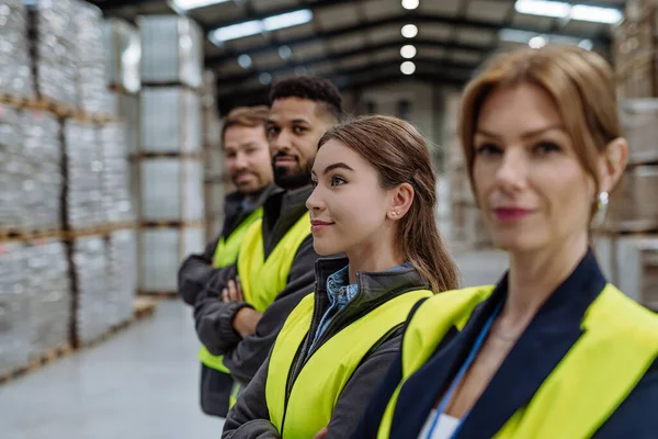 Full team of warehouse employees standing in warehouse. Team of workers in reflective clothing in modern industrial factory, heavy industry, manufactrury. Group portrait.