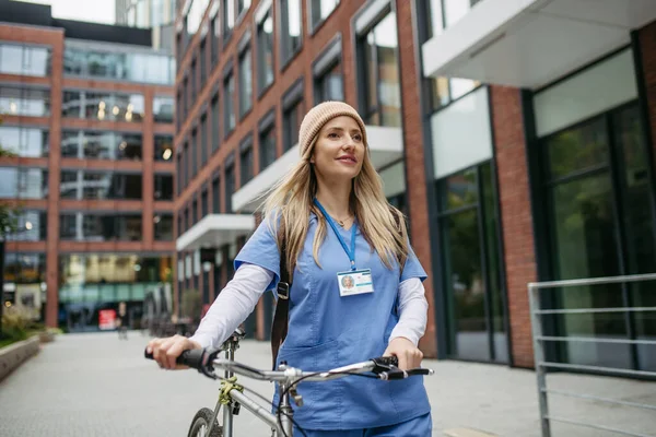 Beautiful nurse commuting through the city by bike. Doctor city commuter traveling from work by bike after long workday in clinic.