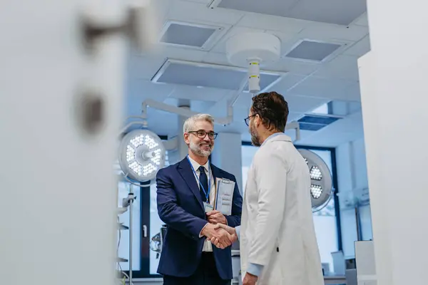 Portrait of pharmaceutical sales representative standing in doctor office, shaking hands. Hospital director, manager of private medical clinic greeting new doctor. Generous donor, giving donation to