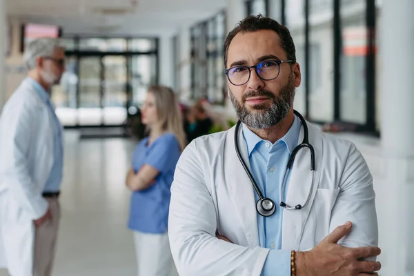 有自信的成熟医生站在医院走廊上的画像 在现代私人诊所里 穿着白色外套 脖子上戴听诊器的英俊医生站在那里 看着相机 — 图库照片