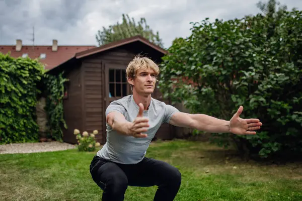 中年男性が伸びて 庭で屋外で運動し スクワットします 自宅でのワークアウトルーチンのコンセプト — ストック写真