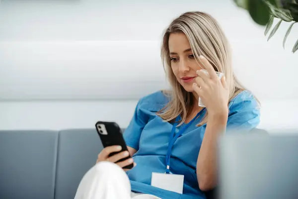 美しい女性医師は 病院での仕事の転換 水を飲んでスマートフォンでスクロール中に休憩を取っています — ストック写真