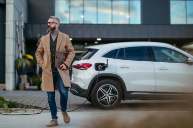 Adam alışverişe gitmeden önce elektrikli arabasını şarj ediyor. Marketin önünde halka açık bir şarj istasyonu. Alışveriş yaparken ücret almak..