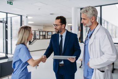İlaç satış temsilcisi tıp binasındaki doktorlarla konuşuyor, tablette yeni ürünler sunuyor. Hastane müdürü, özel klinik müdürü doktorlarla tokalaşıyor..
