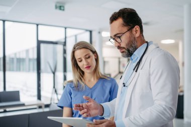 Doktor ve hemşire tabletteki test sonuçlarına bakıp hasta teşhisi hakkında konuşuyorlar. Güzel bir hemşire portresi..