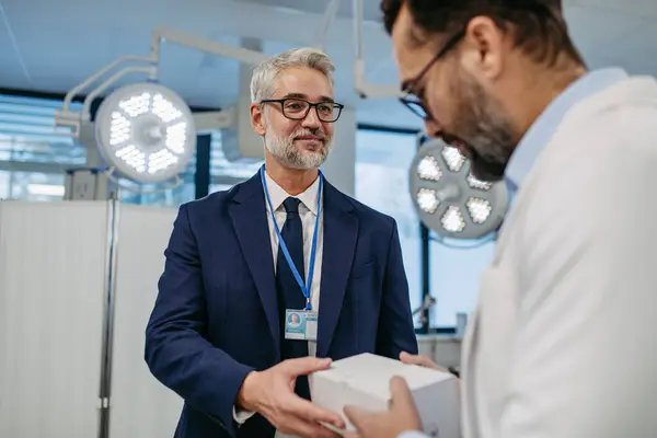 stock image Pharmaceutical sales representative presenting new medication to doctor in medical building, holding box with medication, drugs samples.