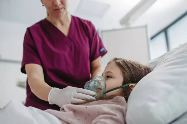 女の子の顔に酸素マスクをかける看護師 彼女の顔に酸素マスクと病院のベッドで子供の患者 — ストック写真
