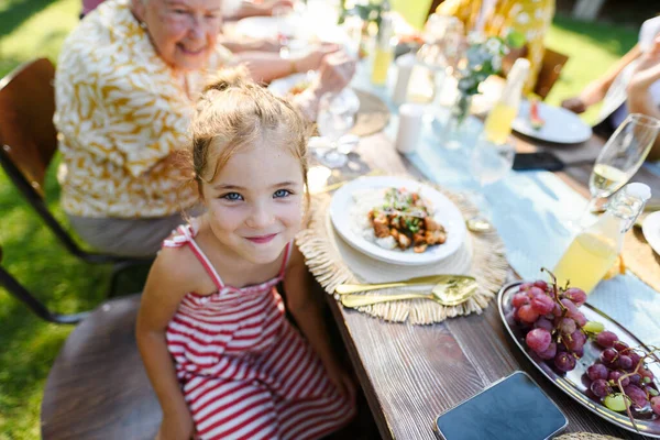 一个漂亮的小女孩坐在餐桌前 在户外吃烤食物的画像 家庭花园派对上的女孩 — 图库照片