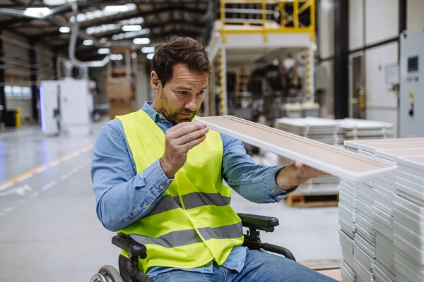 Man in wheelchair working in modern industrial factory, scanning barcodes with scanner. Concept of workers with disabilities, accessible workplace for employees with mobility impairment.