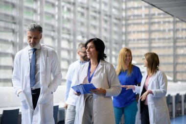 Doktorlar test sonuçlarını tartışıyor, koridorda yürüyorlar. Modern hastane ve klinikte hastaların teşhisini tartışan meslektaşlar.