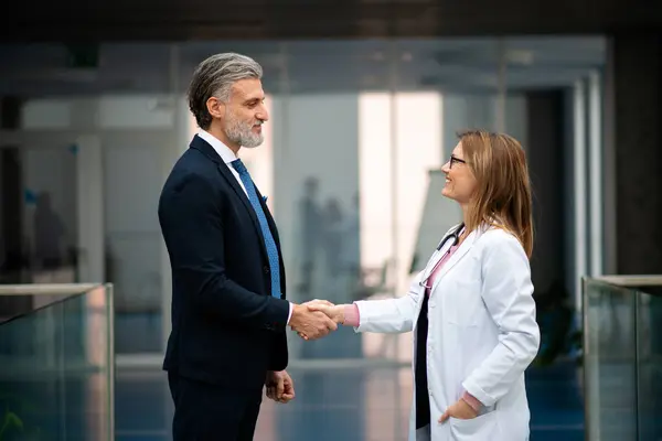 Doctors talking to pharmaceutical sales representative, shaking hands, presenting new pharmaceutical product. Hospital director, manager talking with female doctor. Side view with copyspace.