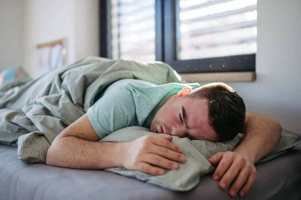 ダウン症候群の若者はベッドで寝ている 腹部に横たわり 寝室で休んでいる — ストック写真