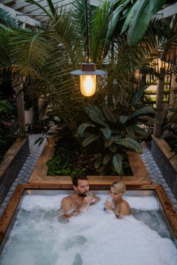 Güzel, olgun bir çift jakuzide dinleniyor, şampanya içiyor, kaplıcada romantik sağlık haftasonunun tadını çıkarıyor. Sevgililer Günü Konsepti.