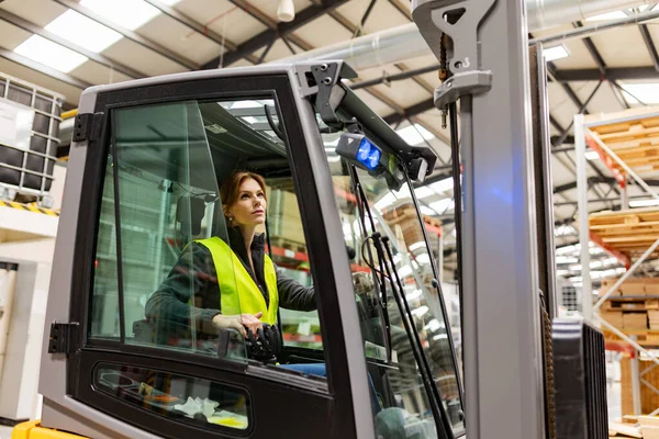 Portrait of female warehouse worker driving forklift. Warehouse worker preparing products for shipmennt, delivery, checking stock in warehouse.