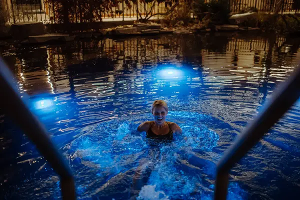 Woman swimming in outdoor pool at night, enjoying calmness and empty pool. Wellness weekend in the hotel.