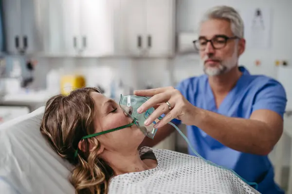 患者の顔に酸素マスクをかける医師 集中治療室で無意識の患者をケアする男性看護師 — ストック写真