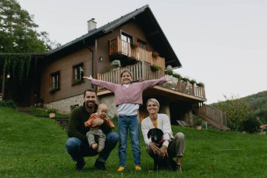 Çatıda güneş panelleri olan bir aile evlerinin önünde duruyor. Güneş enerjisi ve genç bir ailenin sürdürülebilir yaşam tarzı. Yeşil enerji kavramı ve gelecek nesiller için sürdürülebilir gelecek.