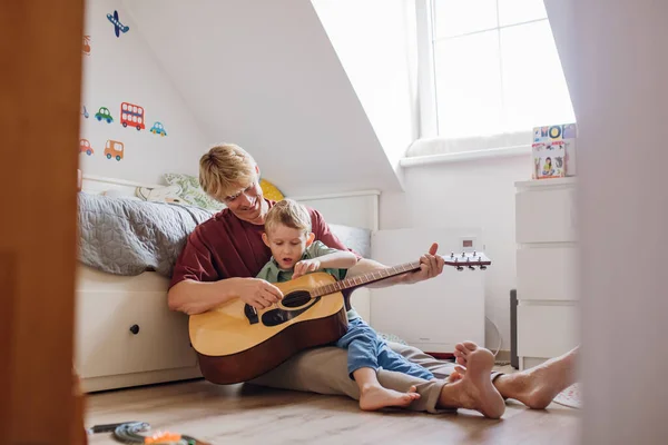 Father teaching boy to play on guitar. Son having fun in their room with dad, playing guitar and singing. Concept of Fathers Day, and fatherly love.