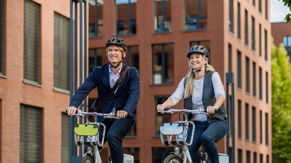 Spouses commuting through the city. Middle-aged city commuters traveling from work by bike after a long workday. Husband and wife riding bikes in city.
