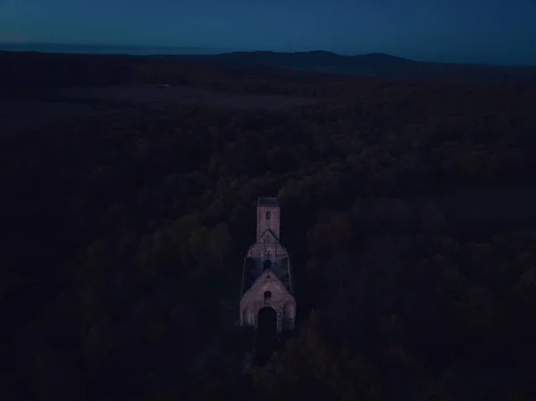 Aerial view of old ruins of historical castle in the middle of forest. Drone view of natural landscape with broken fortress during sunset.