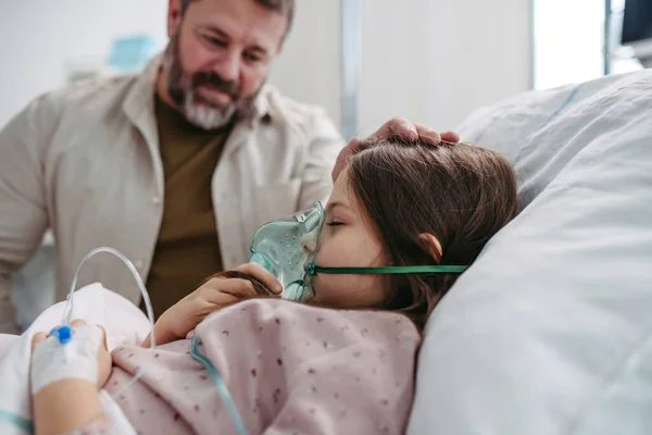父親は病院のベッドで娘の手を握っている Icuで彼女の顔に酸素マスクで病院のベッドにいる子供の患者 — ストック写真