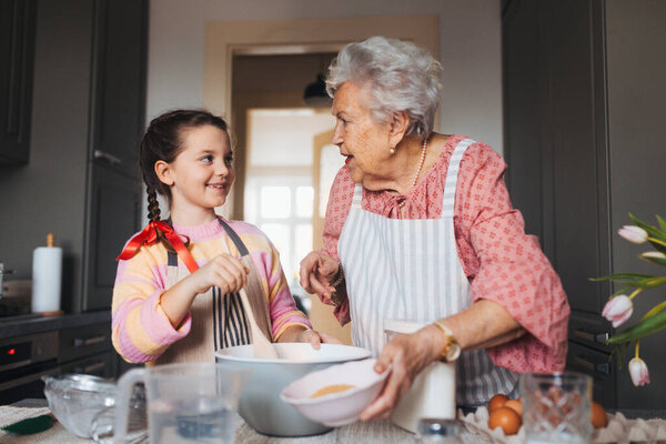Grandmother with grandaughter preparing traditional easter meals, baking cakes and sweets. Passing down family recipes, custom and stories. Concept of family easter holidays.