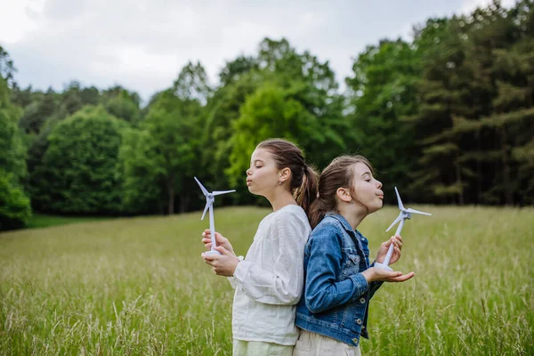 两个女孩拿着模型风力涡轮机 站在草地上 在大自然中 为后代提供替代 可再生能源 绿色能源和可持续生活方式的概念 — 图库照片