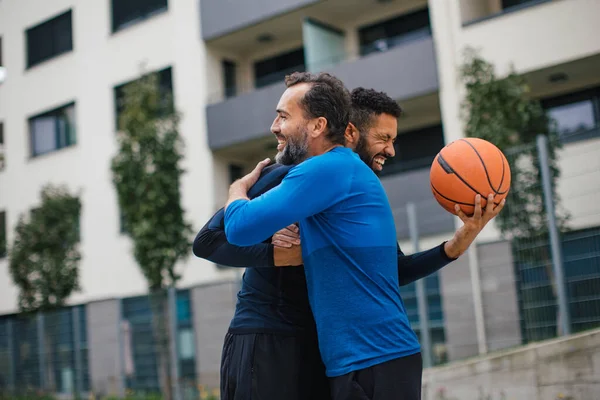 Best friends playing sport outdoors, having fun, hugging after game. Playing basketball at local court, enjoying exercise together. Concept of male friendship, bromance.