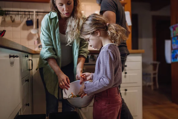 Girl helping parents to put kitchen waste, peel and leftover vegetables scraps into kitchen compostable waste. Concept of composting kitchen biodegradable waste.