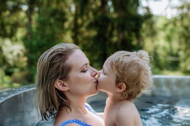 Küçük kızını öpen bir anne. Tahta fıçı jakuzide banyo yapıyor. Yaz tatili konsepti..