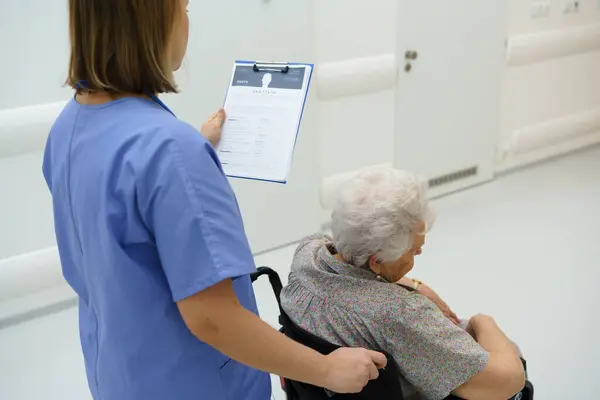 Sjuksköterska Som Knuffar Patienten Rullstol Läser Medicinska Dokument Skrivbordet Patientjournaler — Stockfoto