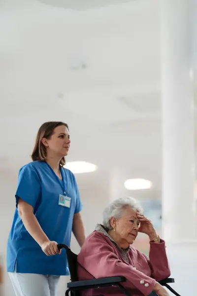 看護師が病院の廊下を横切る車椅子で シニア患者を押した 高齢女性のための感情的なサポート — ストック写真