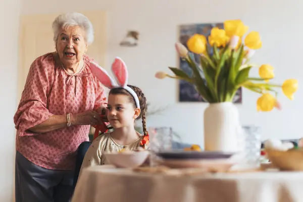 Babička Plete Vnučky Vlasů Dává Červenou Stuhu Copánky Příprava Velikonoční — Stock fotografie