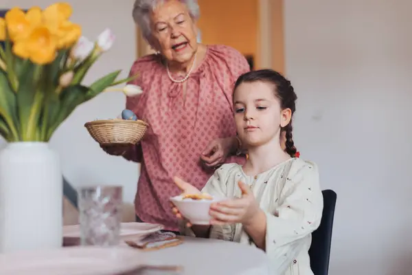伝統的なイースターランチのための孫娘の設定テーブルを持つ祖母 家族の伝統や習慣を再現する 家族のイースターの休日の概念 テーブルで立って祈る — ストック写真