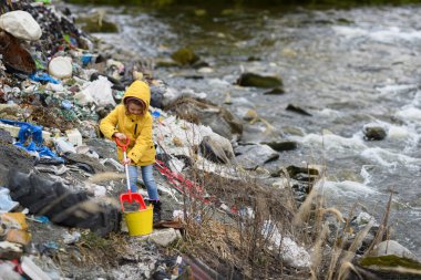 Genç bir kız doğadaki nehir kıyısında çöpleri topluyor. Su ve çevre kirliliği, gelecek nesiller, eko aktivizm kavramı.