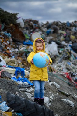 Dünya modelini tutan genç bir kız, toprak dolgusu üzerinde duran, büyük bir atık yığını, doğa kirliliği çevre konsepti ve ekolojik aktivizm. Greta benzeri..