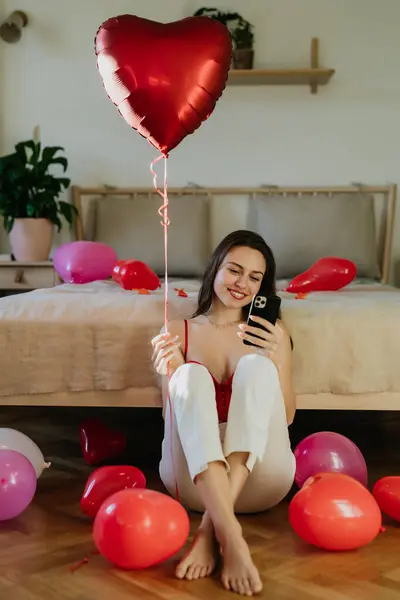Piękna Kobieta Siedząca Przy Łóżku Środku Balonów Przewijająca Się Smartfonie — Zdjęcie stockowe