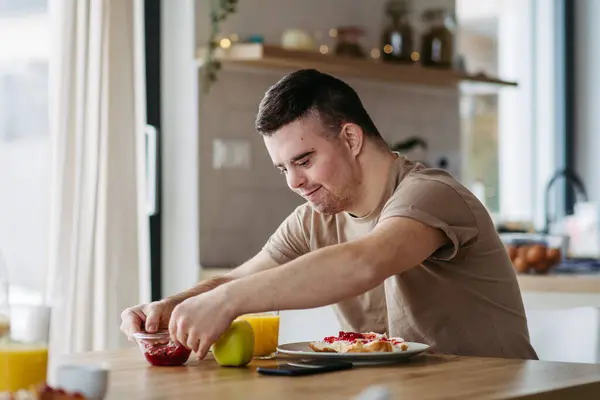Young man with Down syndrome preparing breakfast on his own. Morning routine for man with Down syndrome genetic disorder.