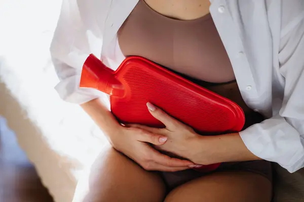年轻女人在家里遭受月经期疼痛 女人用热水瓶加热下腹 子宫内膜异位症 并导致胃痛 靠近点 — 图库照片