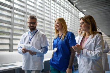 Doktorlar test sonuçlarını tartışıyor, koridorda yürüyorlar. Modern hastane ve klinikte hastaların teşhisini tartışan meslektaşlar.
