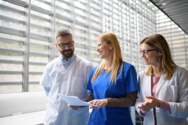 Doktorlar test sonuçlarını tartışıyor, koridorda yürüyorlar. Modern hastane ve klinikte hastaların teşhisini tartışan meslektaşlar.