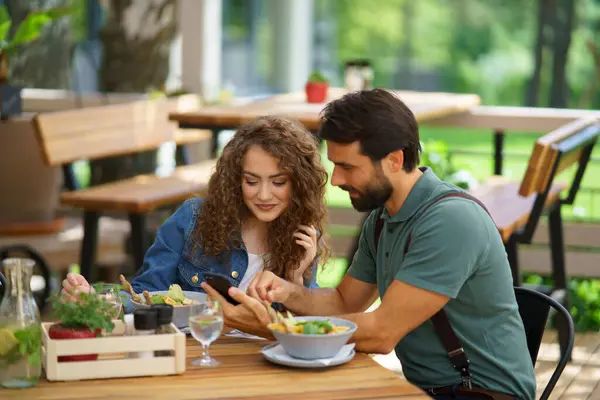 Young couple at date in restaurant, sitting on restaurant terrace. Boyfriend and girlfriend enjoying springtime, having lunch or brunch outdoors, outdoor seating for dining.