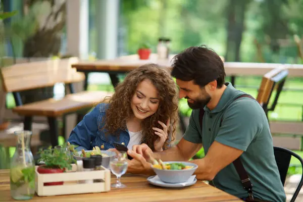 Young couple at date in restaurant, sitting on restaurant terrace. Boyfriend and girlfriend enjoying springtime, having lunch or brunch outdoors, outdoor seating for dining.