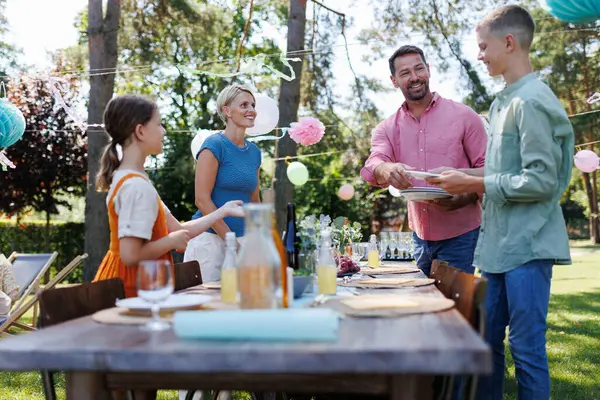 夏の庭のパーティーのための家族の設定テーブル プレート 食べ物 飲み物を持参する — ストック写真