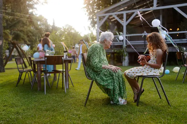 ガーデンパーティーで祖母のためにギターを弾く少女 祖父母と孫の間の愛と親密さ ストック画像
