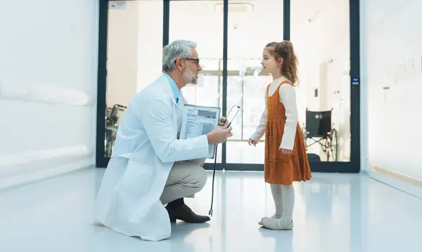 病院のロビーで医者と話している少女 医療従事者と子どもの患者との友好的な関係 ストックフォト