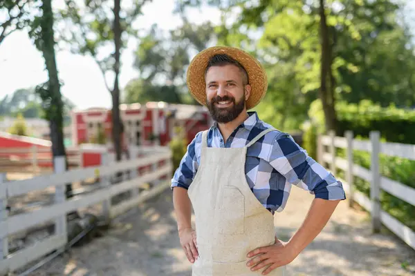木製のフェンスで立っているハンサムな農家の肖像画 家族の牧場で働く帽子を持つ男 ロイヤリティフリーのストック画像