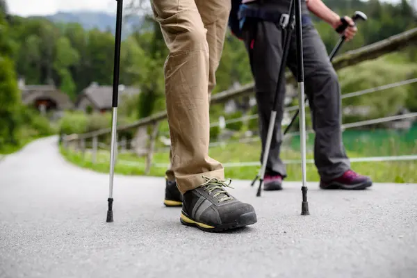 Close up of tourists walking with trekking poles, wearing hikiing boots.