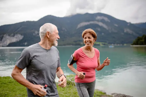 老夫妇在大自然的湖边奔跑 年事已高的丈夫和妻子在山区度过积极的假期 享受体育活动 并在户外放松身心 — 图库照片