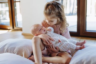 Yeni doğan kız kardeşi tutan ablanın portresi. Kız küçük bebeğe dikkatlice sarılıyor. Kız kardeş sevgisi, yeni aile ferdi için sevinç.